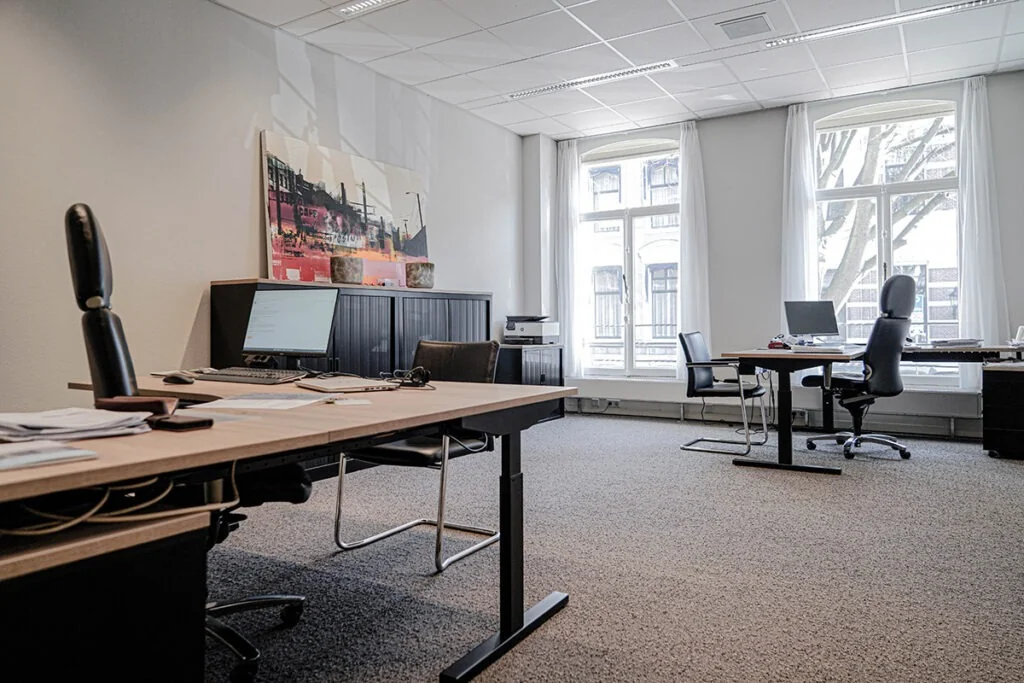 Modern kantoor aan de Burgemeester van Karnebeeklaan met meerdere bureaus, computers en grote ramen met uitzicht op de straat.